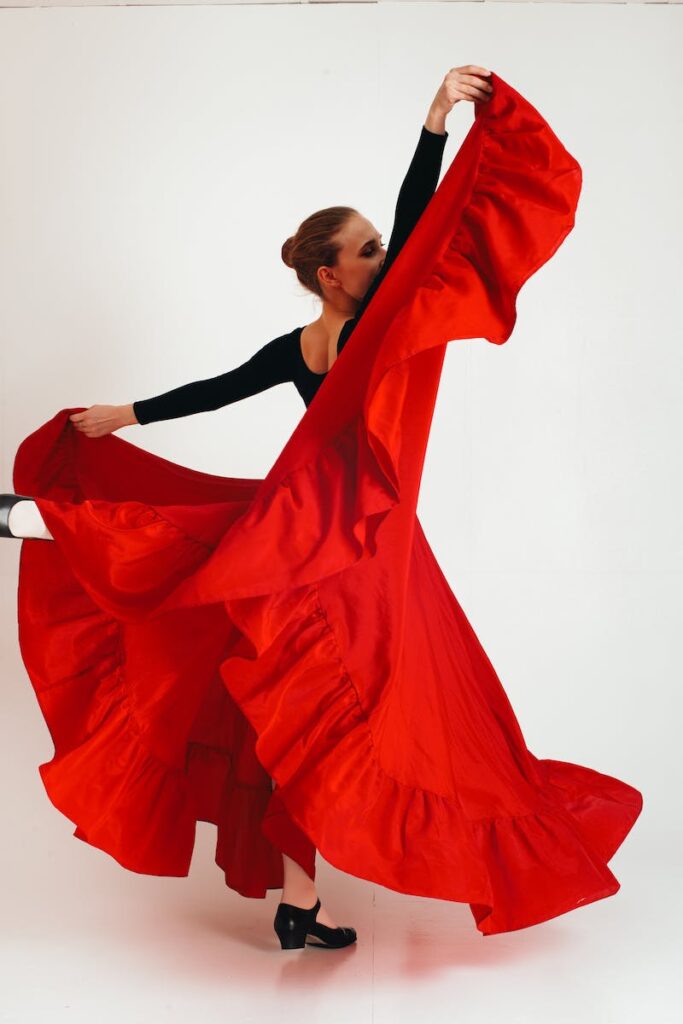 Full body young female flamenco dancer standing with raised leg and hands against white background