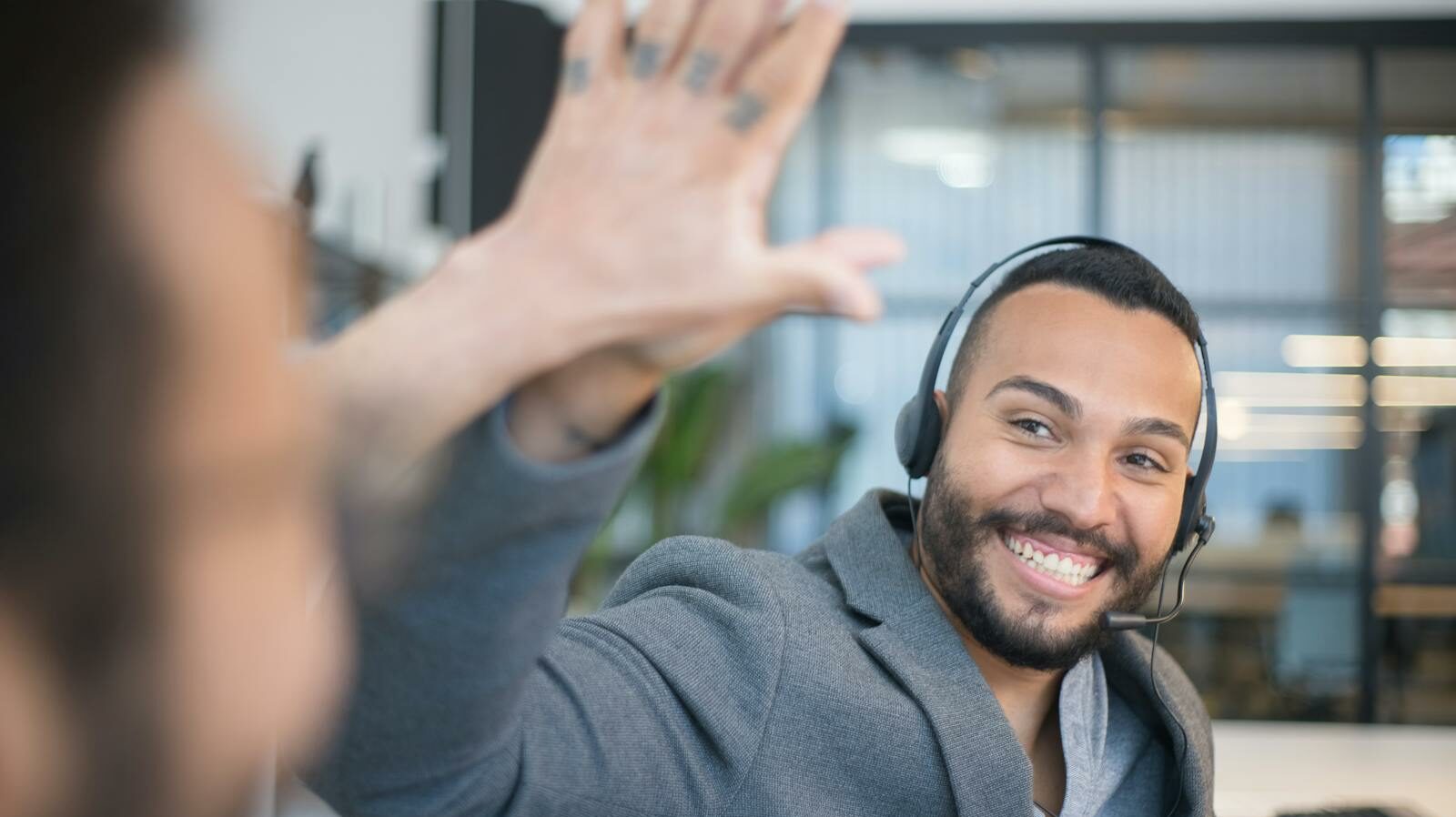 A cheerful call center agent with a headset gives a high five to a colleague in an office.