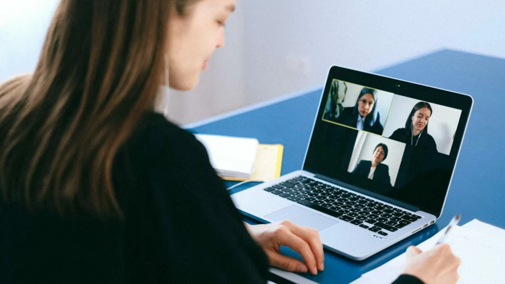 A woman engaging in a video conference using a laptop at home, taking notes.